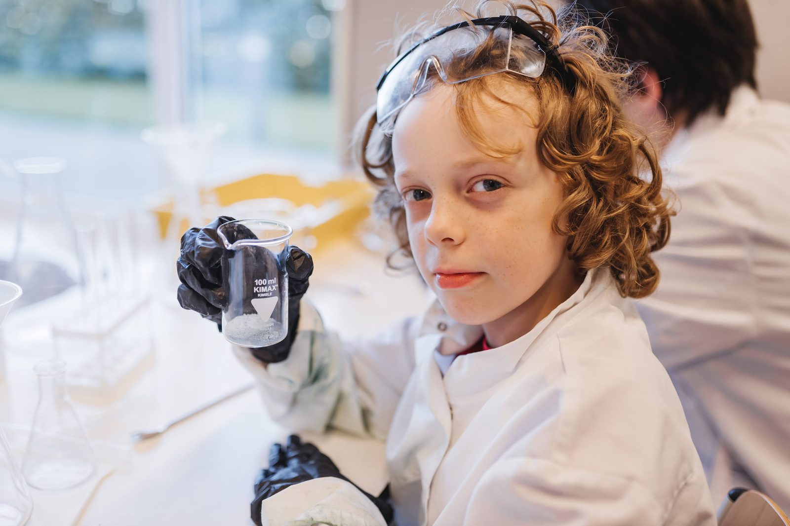 A camper in a lab coat holding a beaker during a MetaMind science lab, EIS Campus